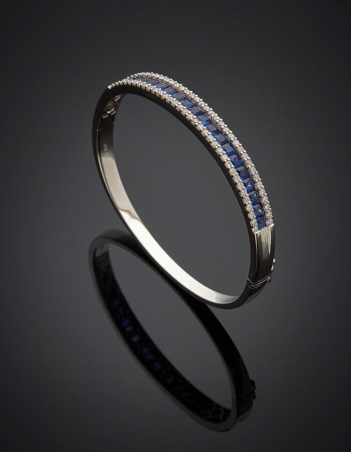 BRACELET rigide ouvrant en or gris (750) centré d'un alignement de saphirs cali…