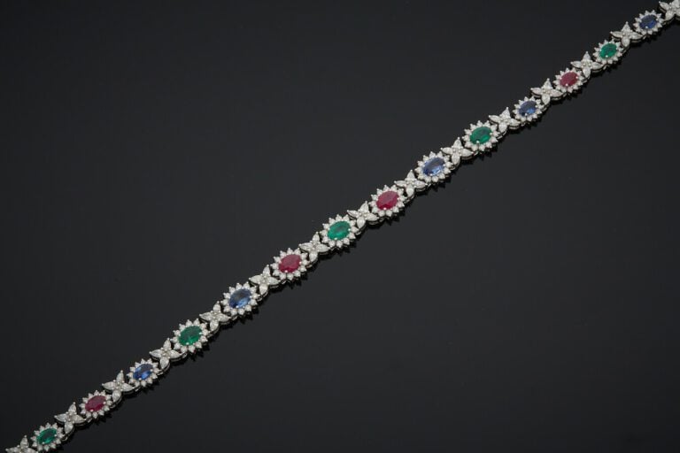 PARURE "marguerites" en or gris (750) articulé, serti de saphirs, rubis et émer…