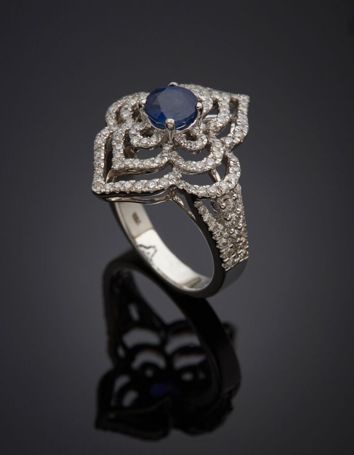 BAGUE "arabesque" en or gris (750‰) ajouré, serti d'un saphir, entouré de diama…