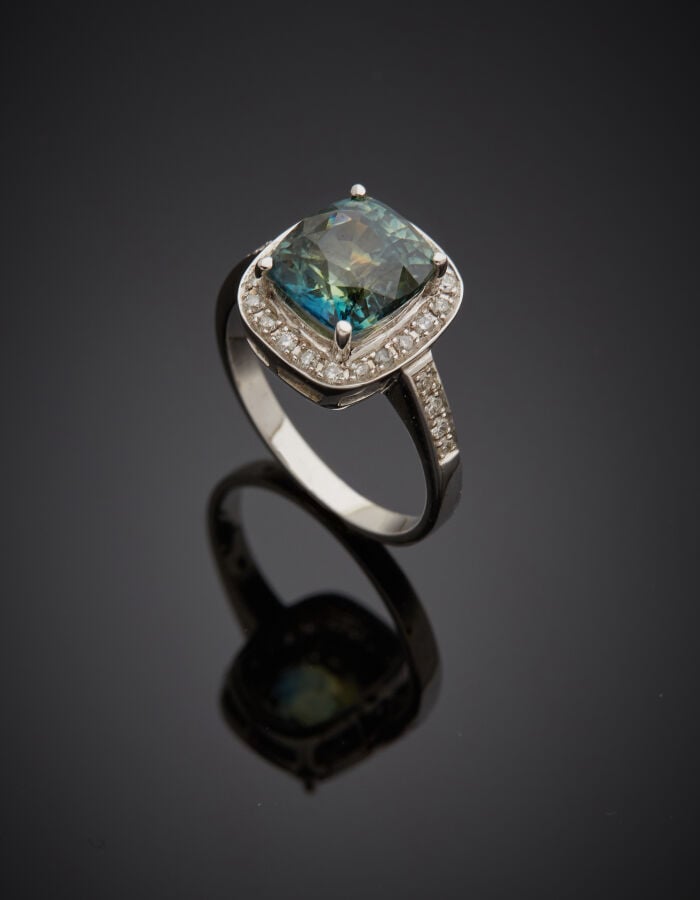 BAGUE en or gris (750‰) serti d'un saphir bleu-vert de forme cousin, entouré et…