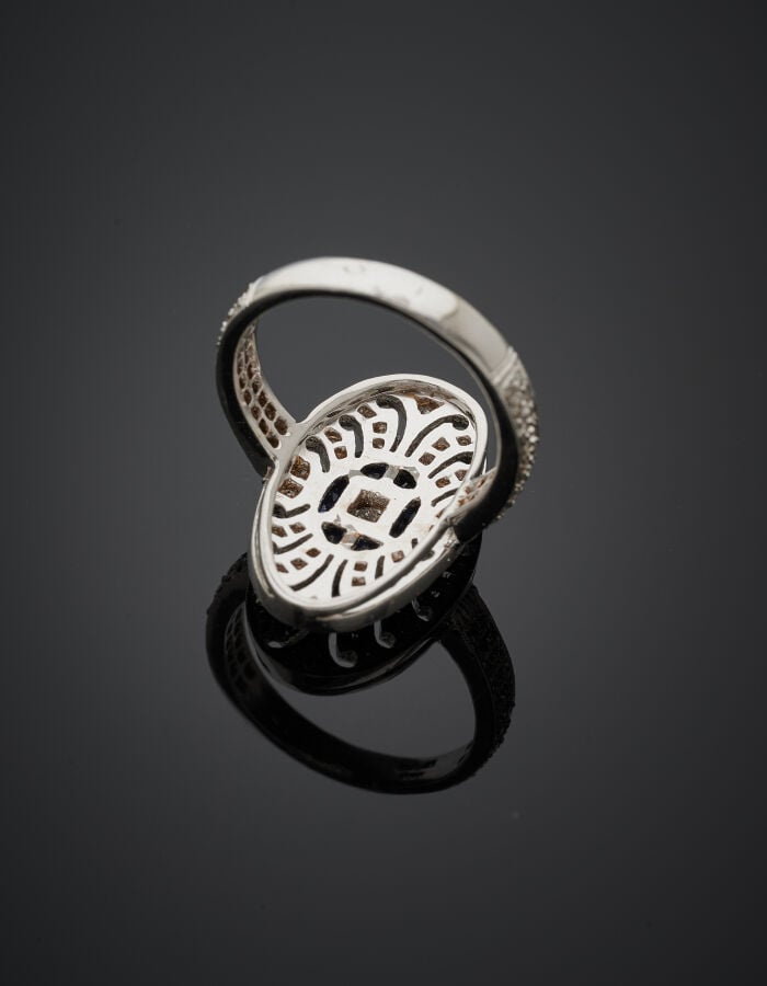 BAGUE ovale en or gris (750‰) ajouré à motifs de volutes, serti d'un diamant ta…