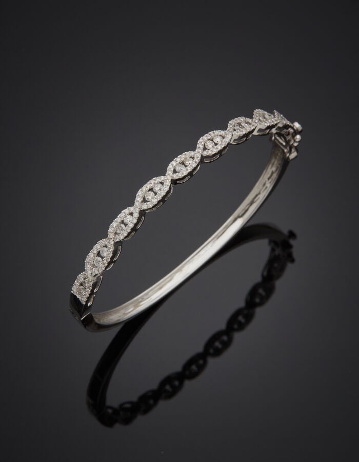 BRACELET rigide ouvrant en or gris (750‰) ajouré à motif tressé, serti de diama…