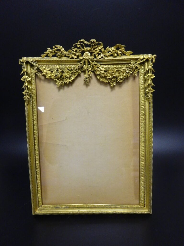 Cadre en bronze doré de forme rectangulaire, le fronton à motifs de noeuds ruba…