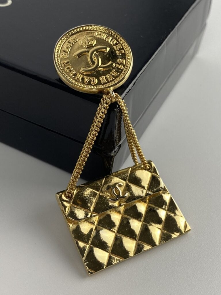 CHANEL - Broche en métal doré formée d'une pièce ornée du sigle de la marque et…