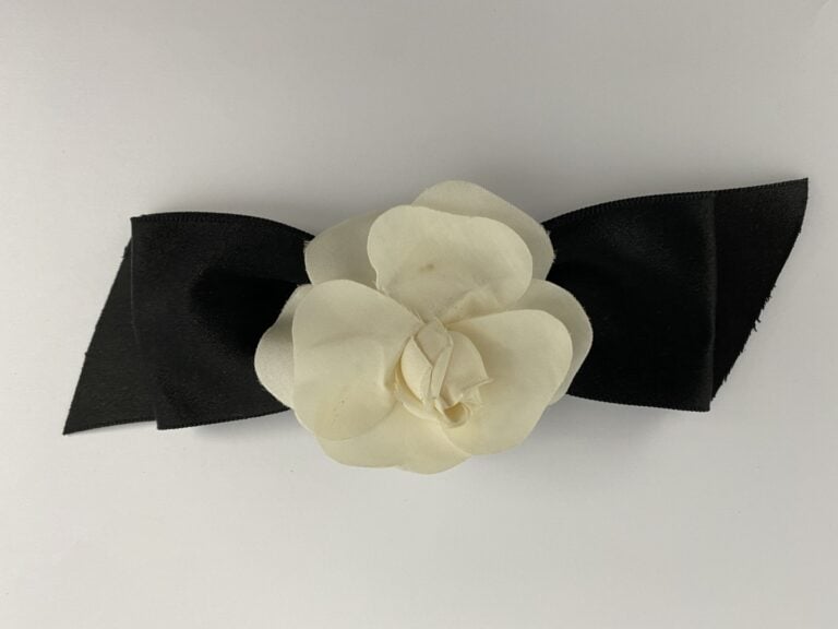 CHANEL - Broche formée d'un noeud en tissu satiné noir orné d'un camélia blanc…