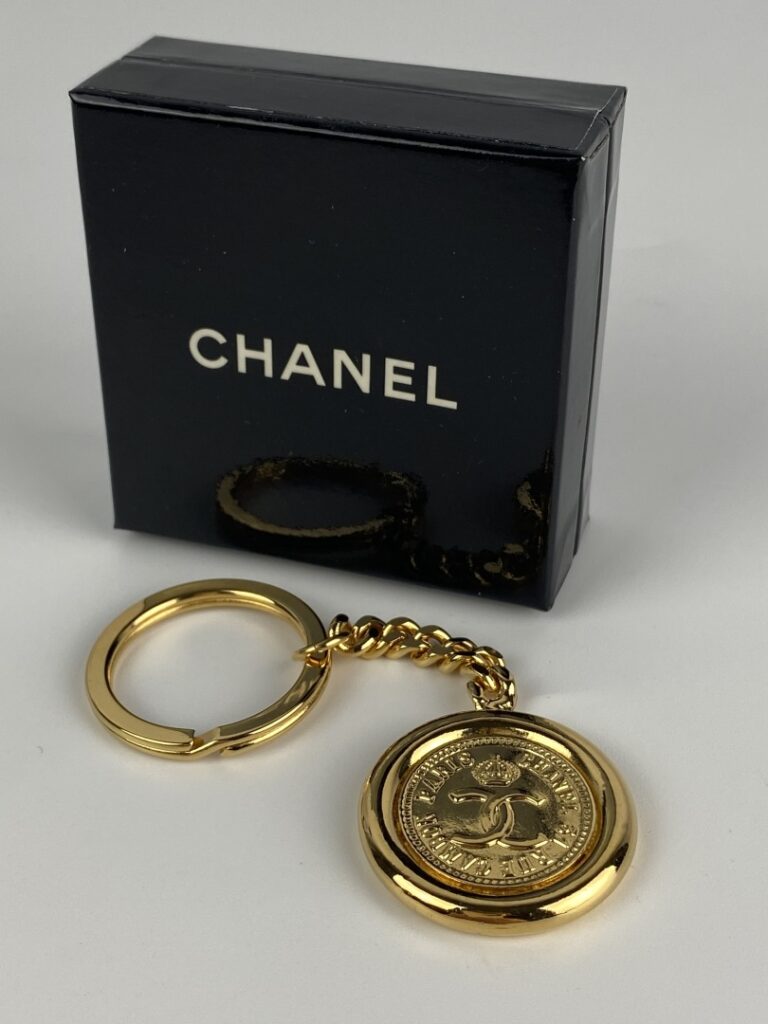 CHANEL - Porte-clé en métal doré orné du profil de Coco Chanel au recto, et du…