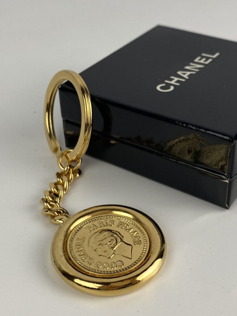 CHANEL - Porte-clé en métal doré orné du profil de Coco Chanel au recto, et du…