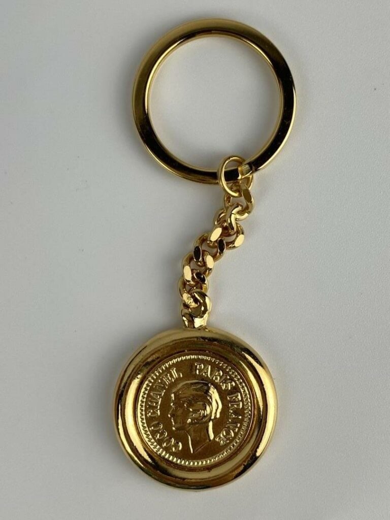 CHANEL - Porte-clé en métal doré orné du profil de Coco Chanel au recto, et du…