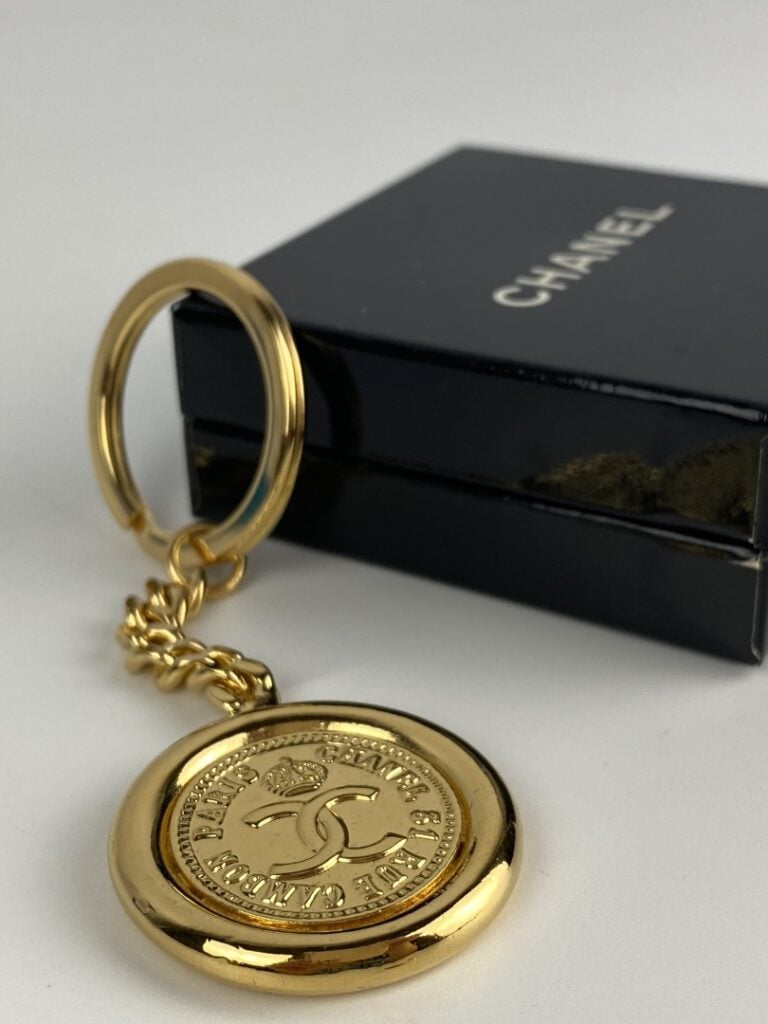 CHANEL - Porte-clé en métal doré orné du profil de Coco Chanel au recto, et du…