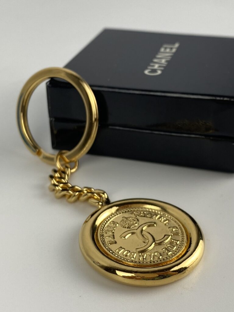 CHANEL - Porte-clé en métal doré orné du profil de Coco Chanel au recto, et du…