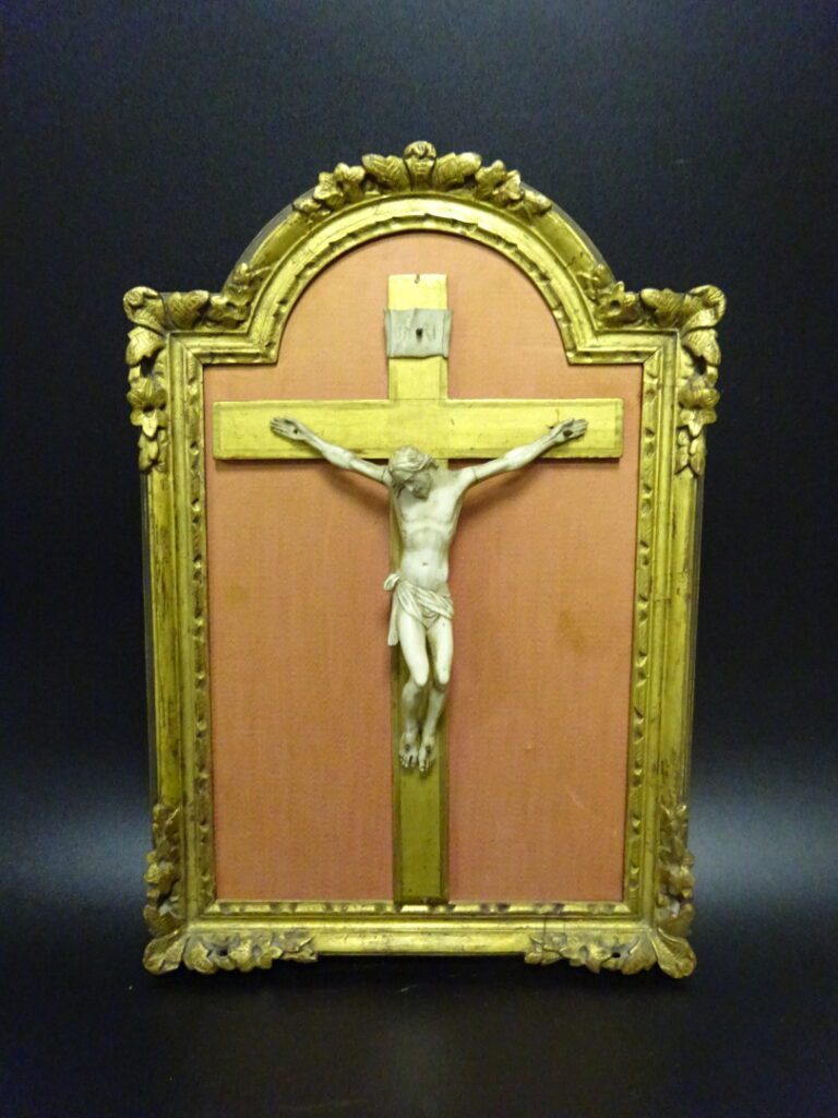 Crucifix en os sculpté, dans un cadre en bois sculpté et doré à fronton cintré.…