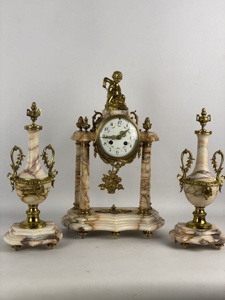 Garniture de cheminée comprenant : une pendule portique surmontée d'un putto et…