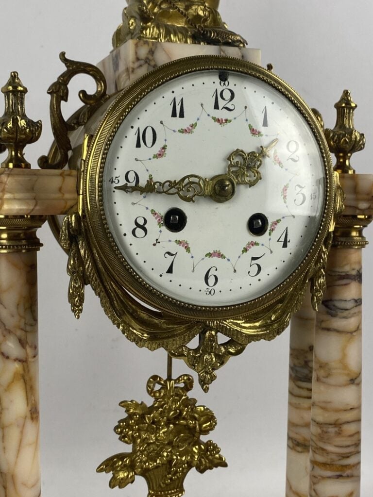 Garniture de cheminée comprenant : une pendule portique surmontée d'un putto et…