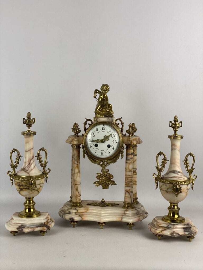 Garniture de cheminée comprenant : une pendule portique surmontée d'un putto et…