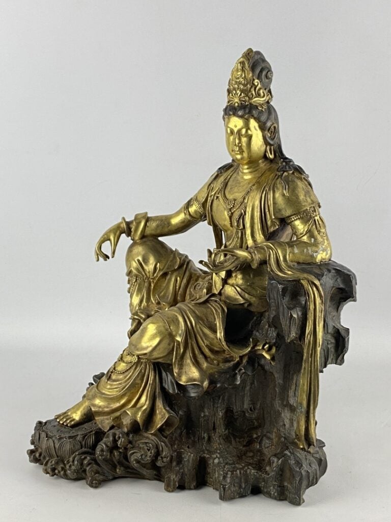 Guanyin en bronze doré - Chine - Représentée assise sur son rocher, la main dro…