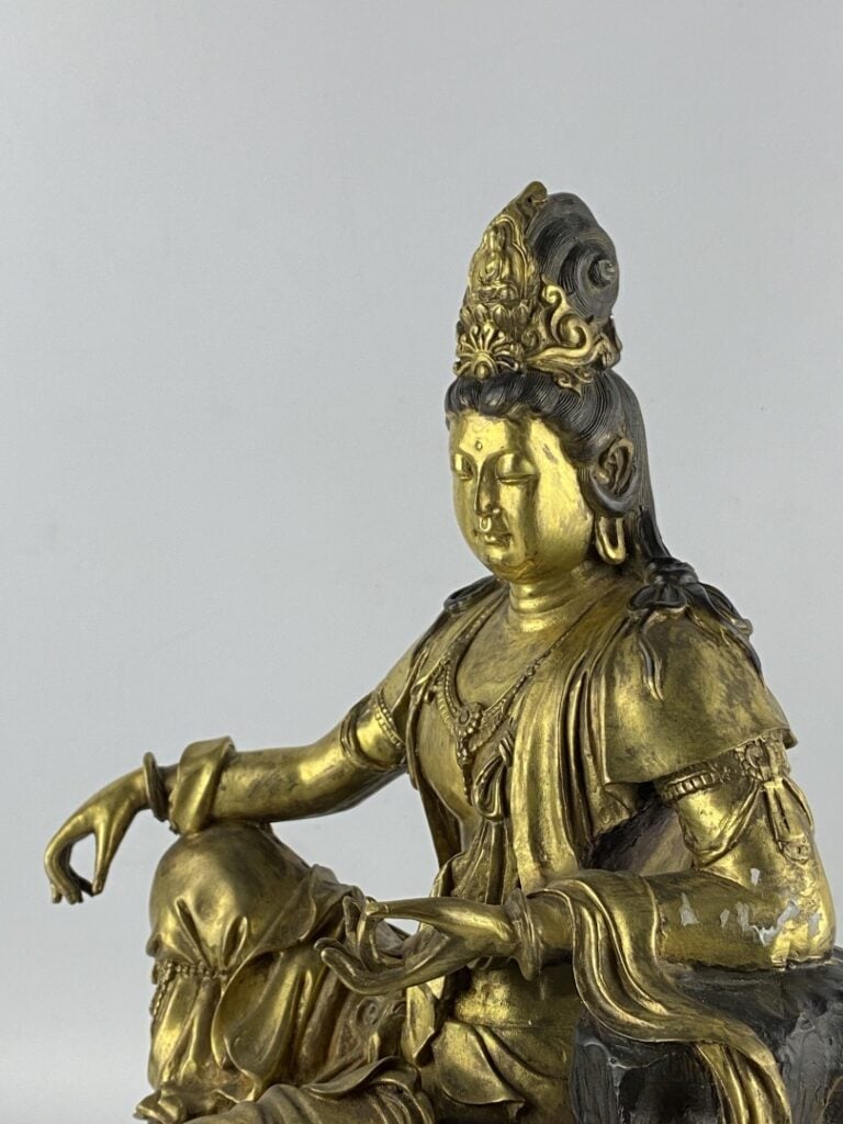 Guanyin en bronze doré - Chine - Représentée assise sur son rocher, la main dro…