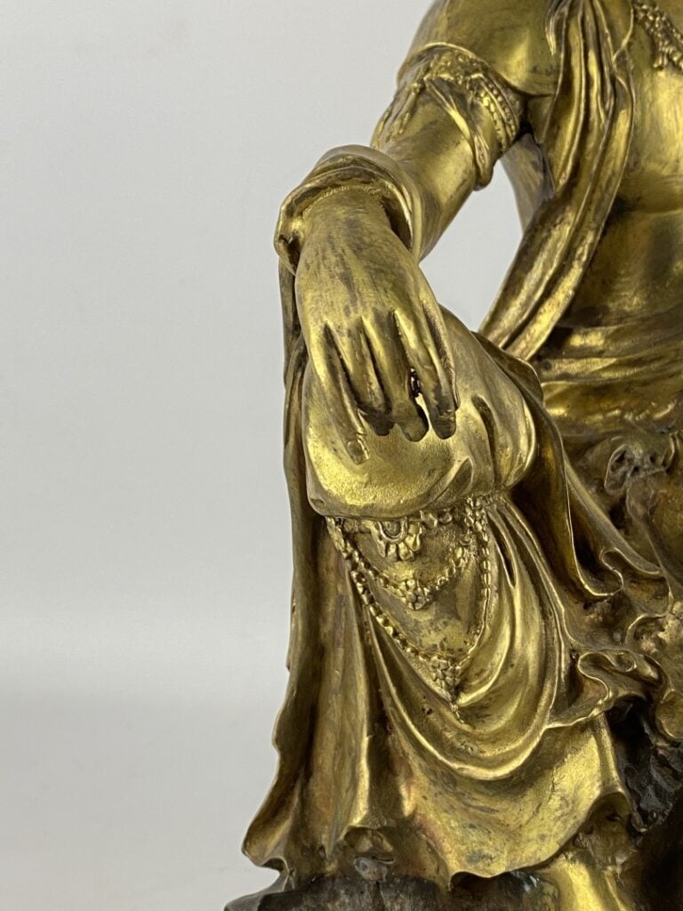 Guanyin en bronze doré - Chine - Représentée assise sur son rocher, la main dro…