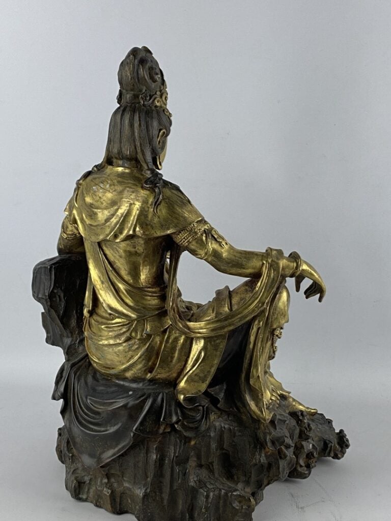 Guanyin en bronze doré - Chine - Représentée assise sur son rocher, la main dro…