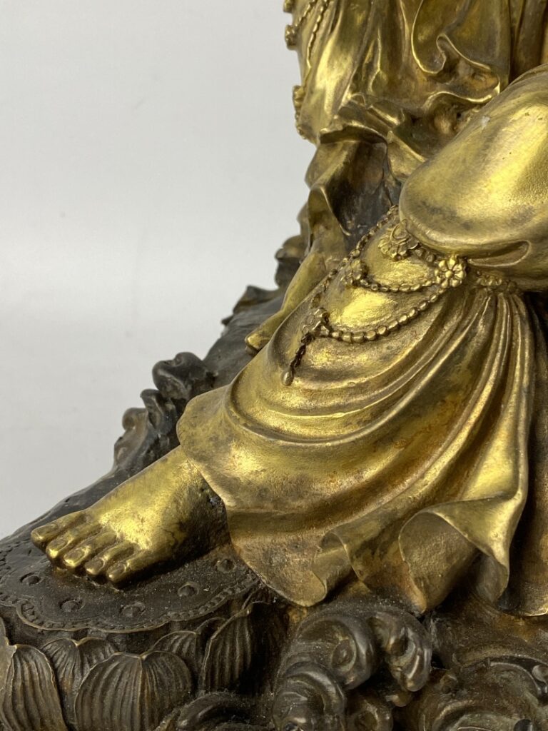 Guanyin en bronze doré - Chine - Représentée assise sur son rocher, la main dro…