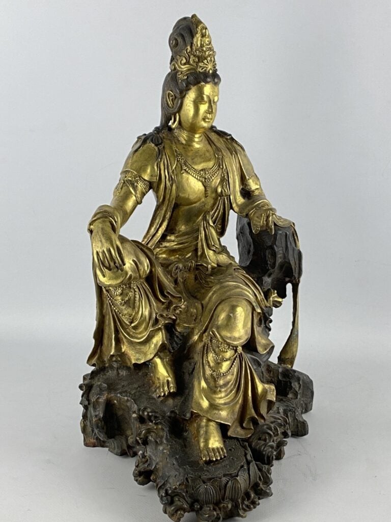 Guanyin en bronze doré - Chine - Représentée assise sur son rocher, la main dro…