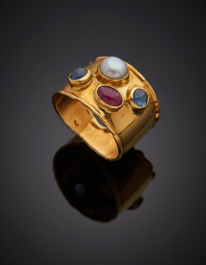 Large BAGUE bordée en or jaune (750‰) serti de deux saphirs, un rubis cabochons…