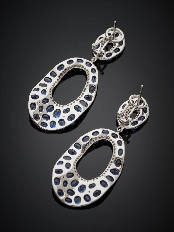 Paire de PENDANTS d'OREILLES en or gris (750‰) ajouré, juponné, pavé de saphirs…