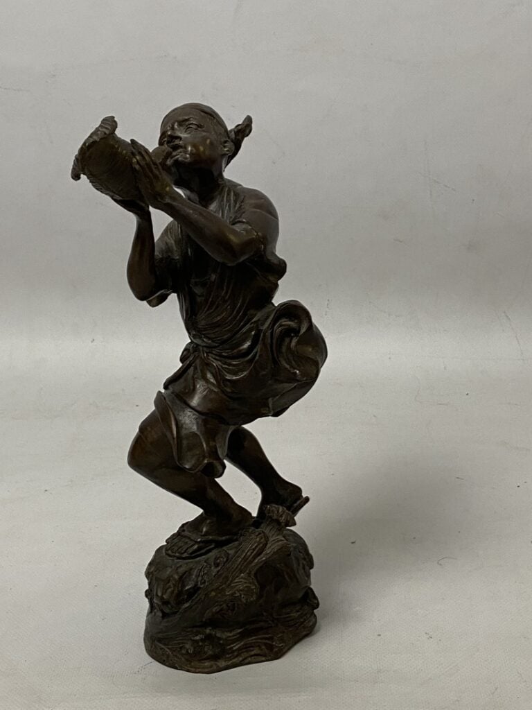 Sujet en bronze à patine brune figurant un homme debout soufflant dans une conq…