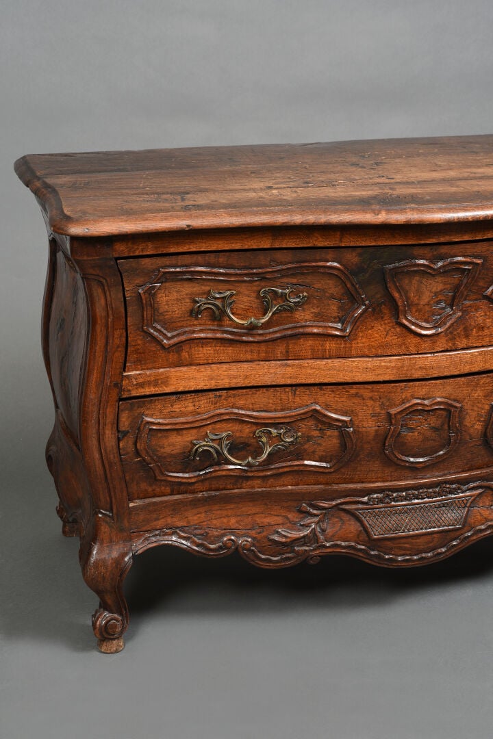 Commode à façade galbée en bois naturel mouluré et sculpté ouvrant à deux tioir…