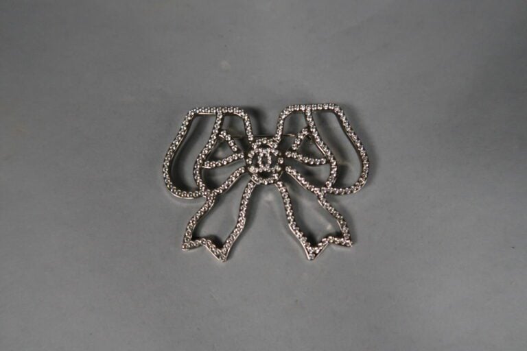 CHANEL - Broche noeud en métal argenté ajouré soulignée de strass - Avec boîte…