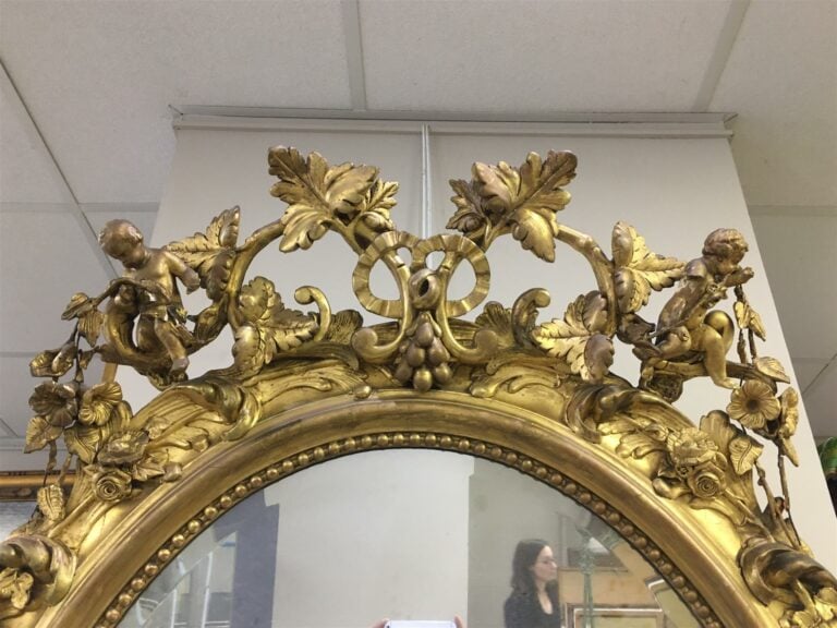 Miroir de forme ovale en bois sculpté, ajouré et doré à décor de fleurs et pamp…