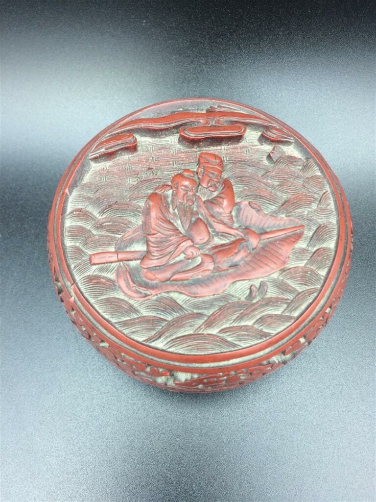 Boite en laque cinabre, à décor en relief sur le couvercle de sages sur une bar…