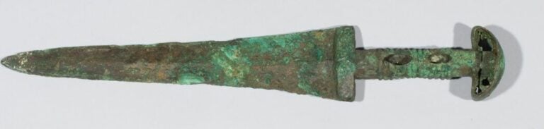 Epée à lame triangulaire et à manche creux annelé. - Bronze à patine verte croû…