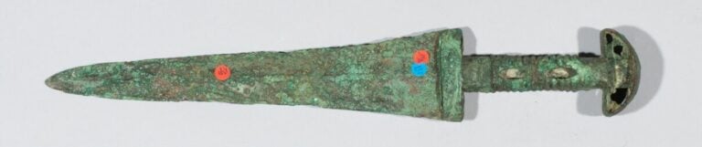 Epée à lame triangulaire et à manche creux annelé. - Bronze à patine verte croû…