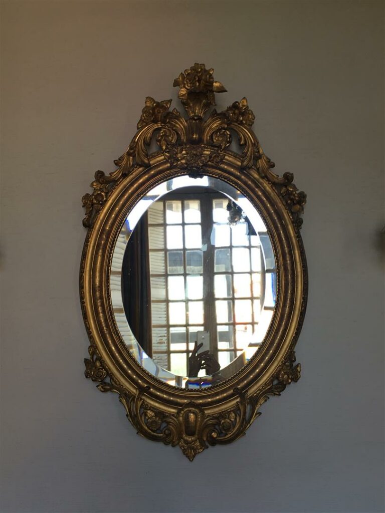 Miroir ovale en bois doré, à décor de volutes fleuries et feuillagées.