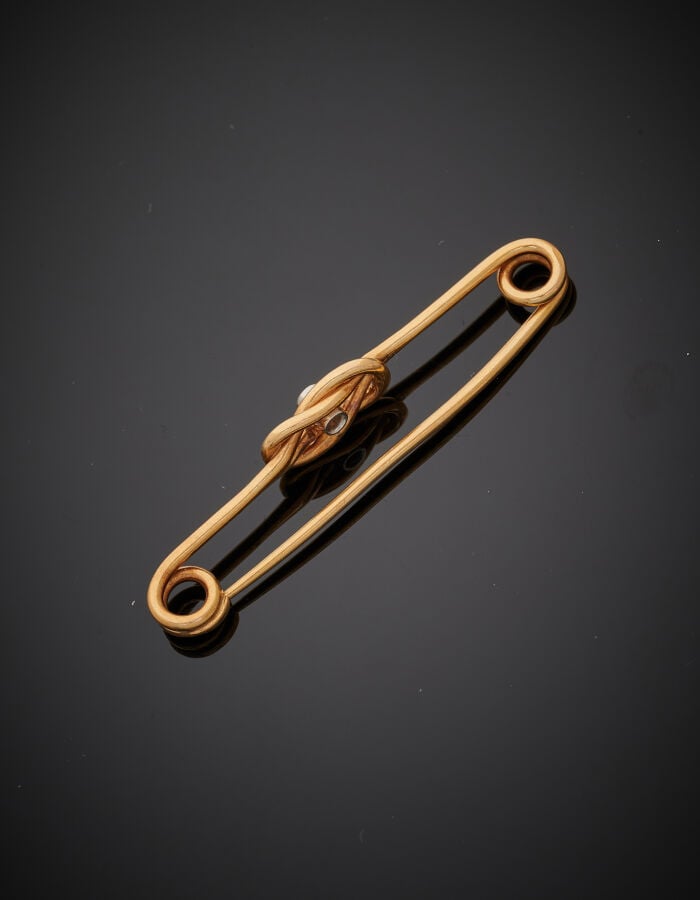 EPINGLE à NOURRICE « noeud » en or jaune (750‰) ajouré, serti d'un diamant tail…