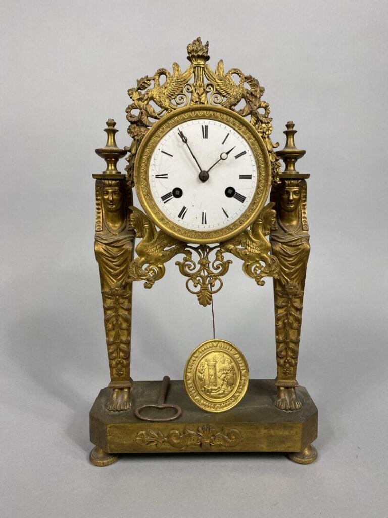 Pendule portique en bronze doré et ciselé. Les montants en forme de cariatydes…