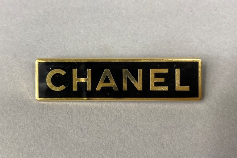 CHANEL - Broche rectangulaire letrtes dorées sur fond noir, signée au dos yann…