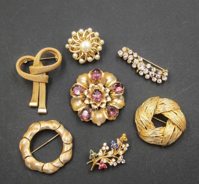 7 broches en métal doré, certaines ornées de pierres de couleur ou fausses perles, dont une TRIFAR