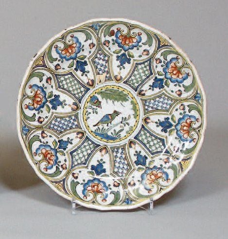 Assiette à bord contourné, décor polychrome au centre d'un oiseau branché dans une réserve cernée de croisillons et coquilles fleuries formant rosac
