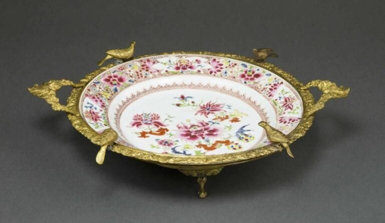 ASSIETTE CREUSE EN PORCELAINE DE LA COMPAGNIE DES INDES A MONTURE DE BRONZE DORE AUX OISEAUX Chine de Commande / pour l'export, Dynastie Qing, Epoque XVIIIe siècle Elle est ornée en émaux polychromes de la "Famille Rose", dans le cavetto d'une composition florale cerclée d'une frise de festons, sur l'aile d'un fond tapisson floral et de quatre médaillons laissés en réserve, eux-mêmes centrés de fleur