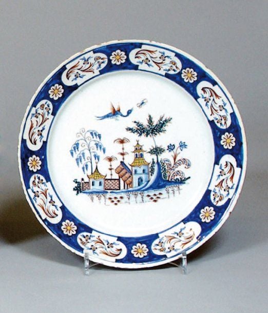 Assiette, décor polychrome au centre de pagodes, rochers fleuris, volatiles et sur l'aile de réserves de fleurs se détachant sur un fond bleu fleur