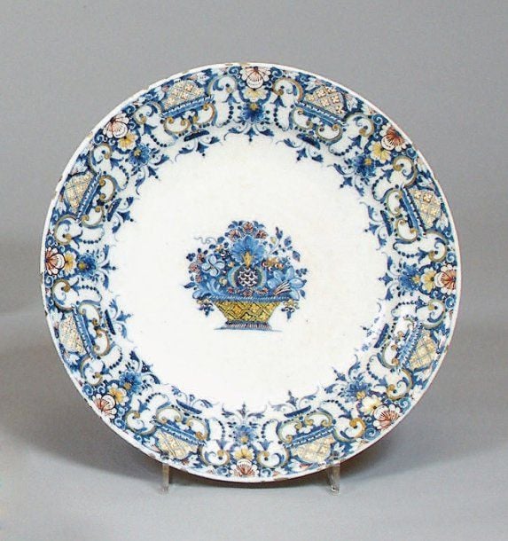 Assiette décorée en bleu, ocre et rouge de fer, au centre d'un panier fleuri et sur l'aile de larges lambrequins fleuris rayonnant