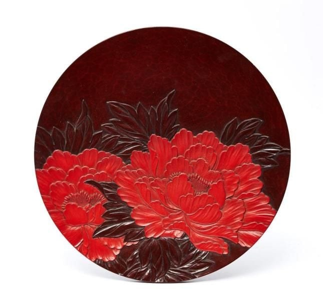 Assiette plate laquée décorée d'un motif gravé figurant des pivoines de couleur rouge-foncé et vermillo