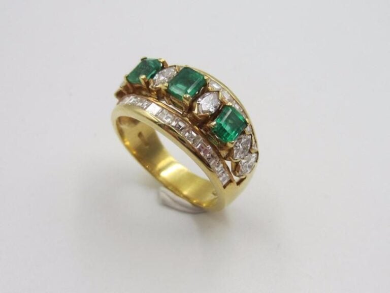 BAGUE « bandeau » en or jaune (750 millièmes) ajouré serti de trois émeraudes rectangulaires alternées de diamants navettes et soulignés de diamants taille princess