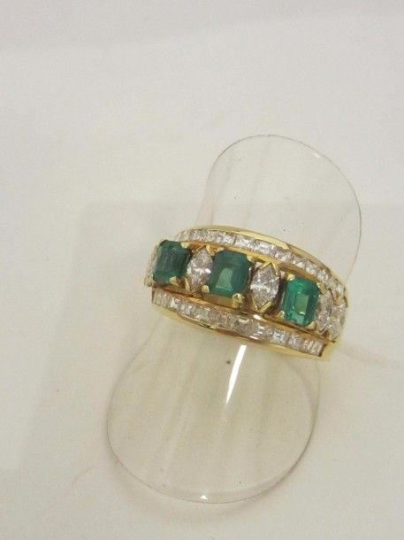 BAGUE « bandeau » en or jaune (750 millièmes) ajouré serti de trois émeraudes rectangulaires alternées de diamants navettes et soulignés de diamants taille princess