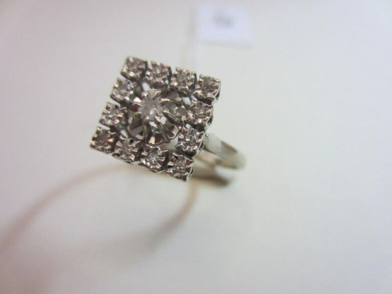 BAGUE «carrée» en or gris (750 millièmes) serti d'un diamant taille brillant entouré d'un motif juponné et de diamants taille 8/