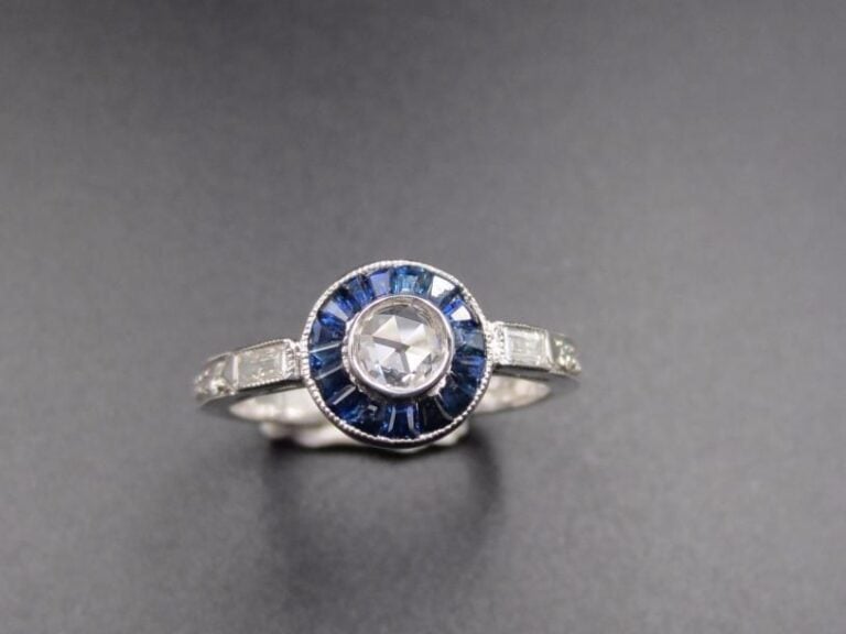 BAGUE « circulaire » en or gris (750 millièmes) serti d’un diamant taillé en rose entouré de saphirs calibrés épaulés de deux diamants baguette et taille brillan