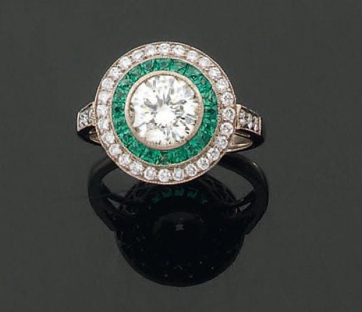 BAGUE circulaire en or gris serti au centre d'un diamant de taille brillant et d'un double entourage d'émeraudes calibrées et de diamant