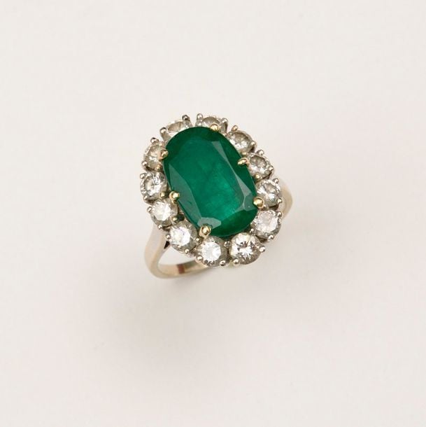 BAGUE en or blanc sertie d’une émeraude ovale à pans coupés dans un entourage de douze diamants ronds de taille brillan
