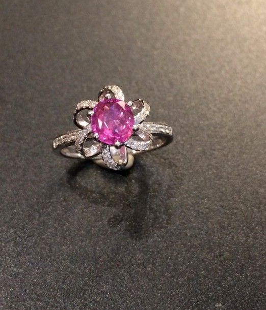BAGUE en or gris (750 millièmes) ajouré à motif de volutes serti d’un saphir rose pesant 1,10 carat, de forme ovale, entouré et épaulé de diamants taille brillan